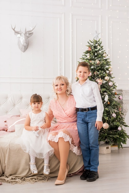 Mãe com filha e filho no fundo de uma árvore de Natal.