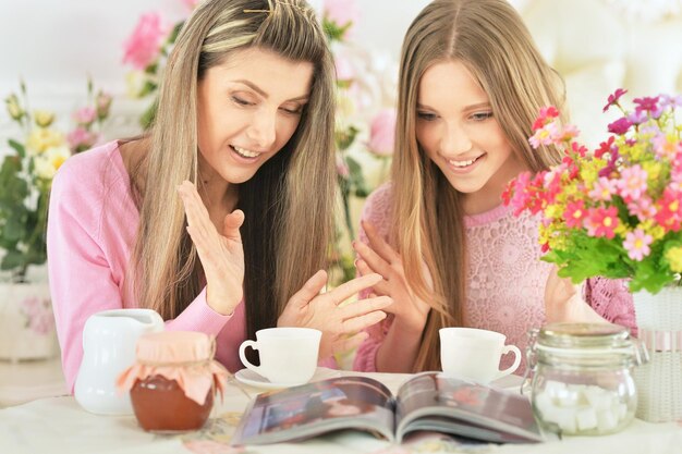 Mãe com filha lendo revista e bebendo chá