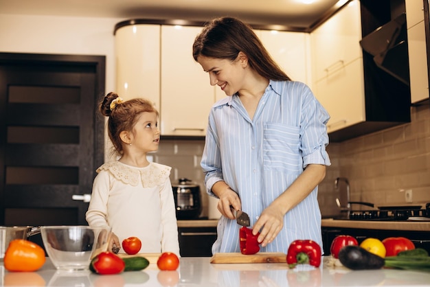 Mãe com filha preparando salada de legumes frescos na cozinha