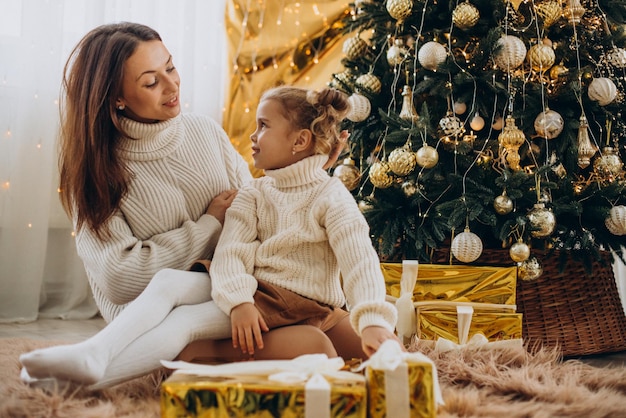 Mãe com filha segurando presente de Natal sob a árvore de Natal