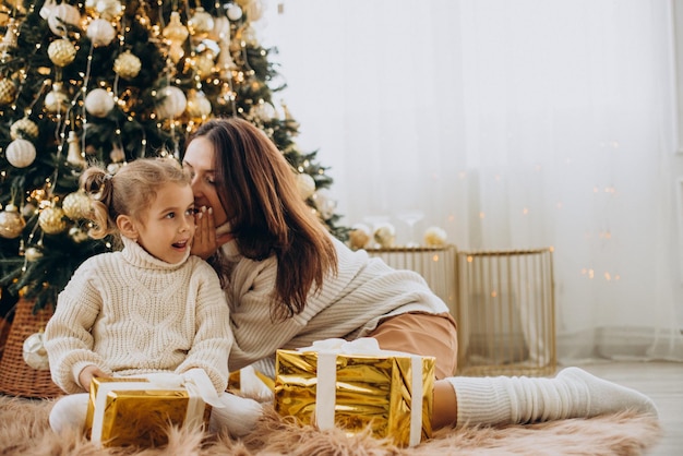 Mãe com filha segurando presente de Natal sob a árvore de Natal