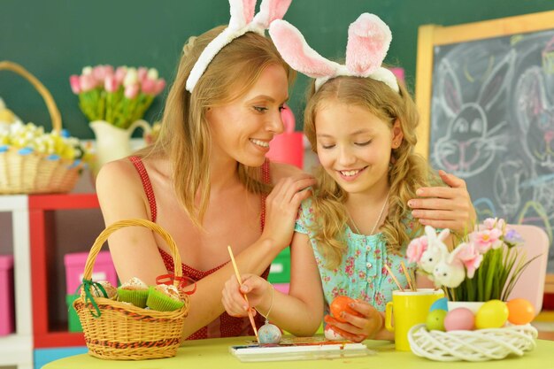 Mãe com filha usando orelhas de coelho decorando ovos de Páscoa