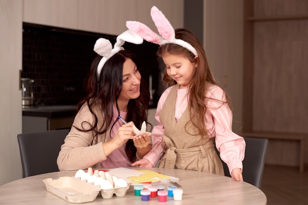 Mãe com filha usando orelhas de coelho e decorando ovos de Páscoa em casa