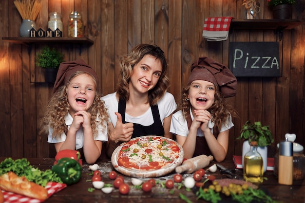 Mãe com filhas cozinhar pizza na cozinha