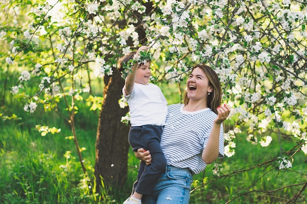 Mãe com filho bebê no jardim primavera durante a hora de ouro Mãe e filho são ativos na natureza Família caminha em um jardim primavera Feliz dia das mães