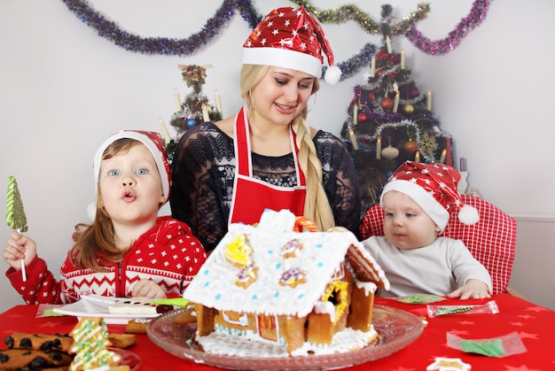 Mãe com filho e filha decoram casa de pão de gengibre