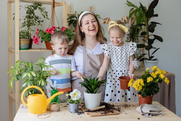 Mãe com filho e filha em jejum, planta ou transplante flores de interior Ajudante nas tarefas domésticas