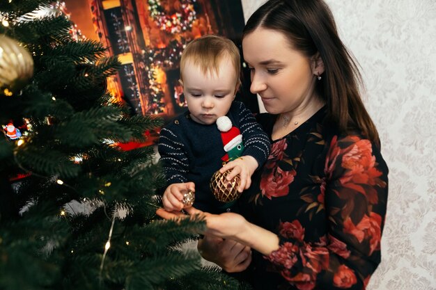 Mãe com filho menino criança fofa criança brincalhona sentada perto da árvore de natal brincando