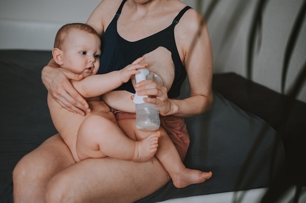 Mãe com filho recém-nascido segurando-o nos braços usando bomba tira leite abraços