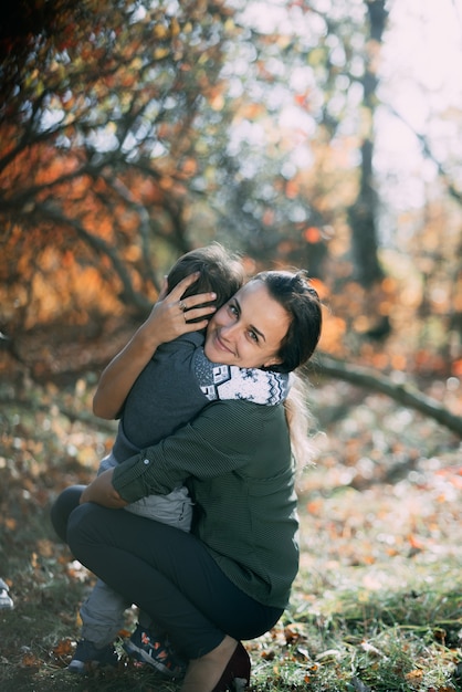 Mãe com filho três anos no outono na floresta, abraço e ternura