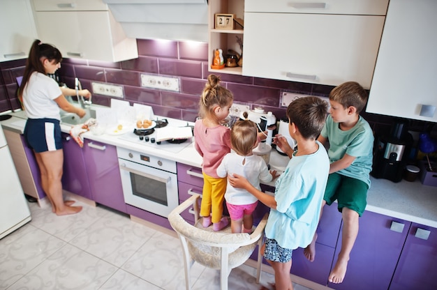 Mãe com filhos cozinhando na cozinha, momentos infantis felizes.