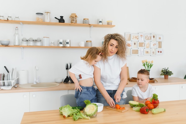 Mãe com filhos preparando salada de legumes em casa