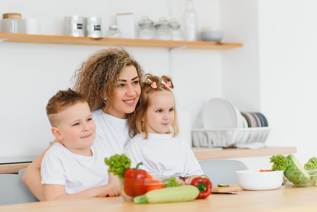 Mãe com filhos preparando salada de legumes em casa