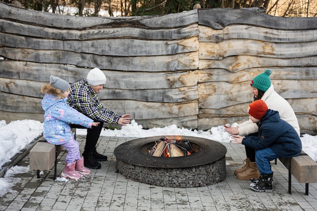 Mãe com filhos sentados perto da fogueira do acampamento no inverno na floresta Crianças no campo