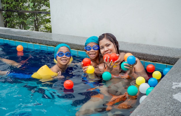 Mãe com os filhos brincando de bola na piscina