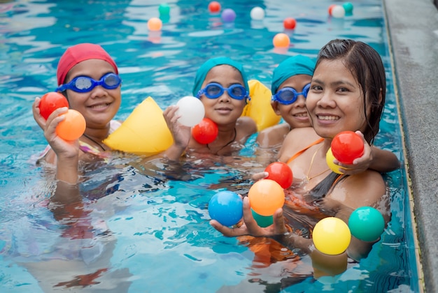 Mãe com os filhos brincando de bola na piscina