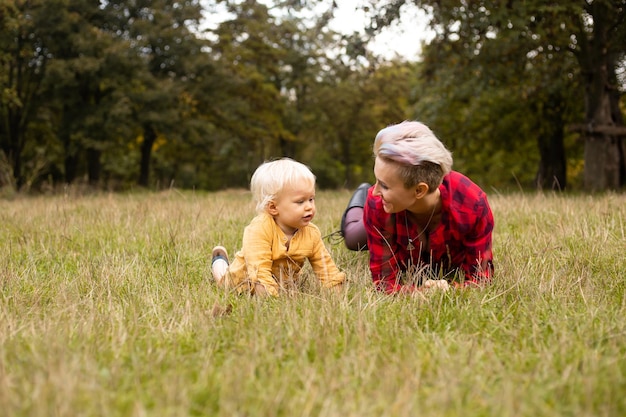 Mãe com seu filho bebê deitado no prado na grama no outono ou verão