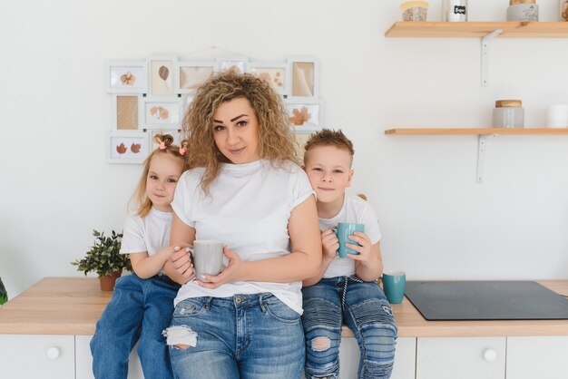 Foto mãe com seus dois filhos sentados na mesa da cozinha.