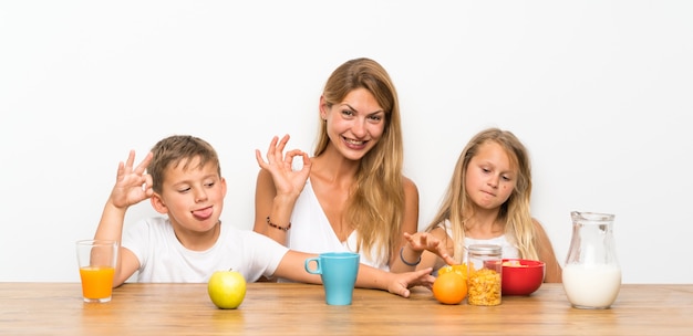 Mãe com seus dois filhos tomando café e fazendo sinal de OK