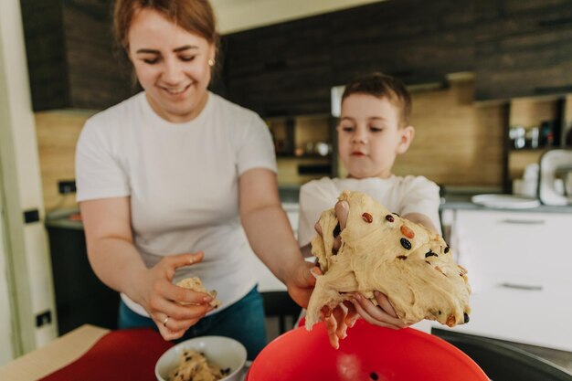 Mãe com seus filhos pequenos à mesa na cozinha em casa preparando juntos a massa para assar um bolo de férias