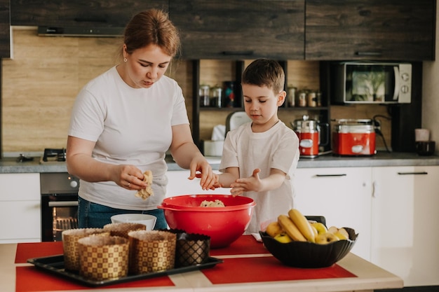Mãe com seus filhos pequenos à mesa na cozinha em casa preparando juntos a massa para assar um bolo de férias