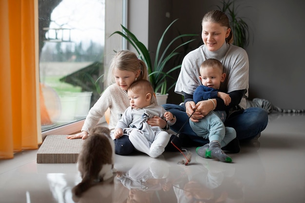 mãe com seus três filhos brincando com um gato no chão de casa