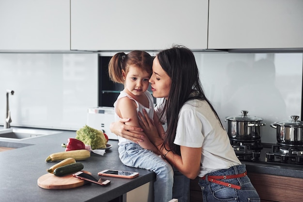 Mãe com sua filha abraçando-se dentro de casa na cozinha