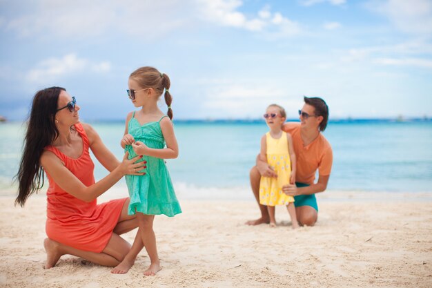 Mãe com sua filha mais velha em primeiro plano e pai com filha mais nova em segundo plano na praia