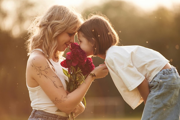 Mãe com sua filha pequena está no campo com flores vermelhas