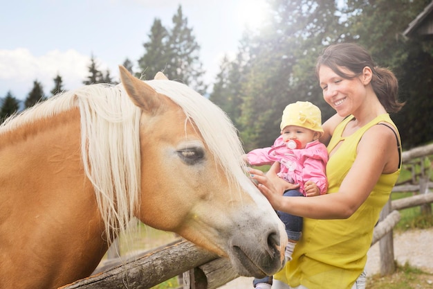 Mãe com sua filha se divertindo no rancho da fazenda e conhecendo um cavalo Conceito de terapia de animais de estimação no campo com cavalo na fazenda educacional Conceito de terapia de cavalos com crianças