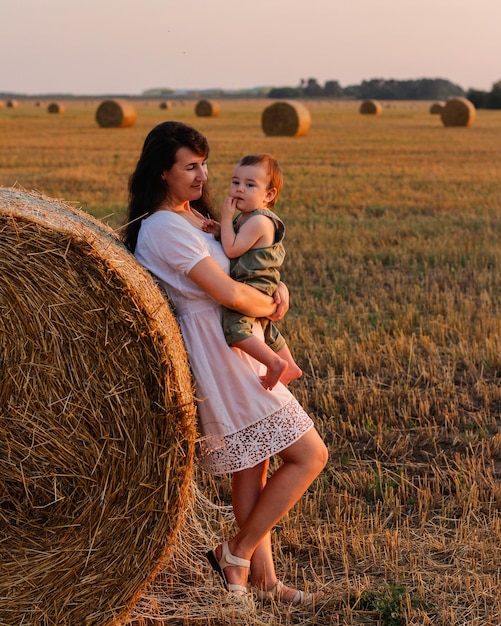 Mãe com um bebê nos braços em um campo ao pôr do sol Conceito de família feliz e férias de verão