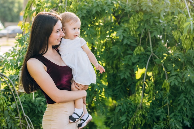 Mãe com um bebê nos braços em um dia ensolarado caminha pelo parque.