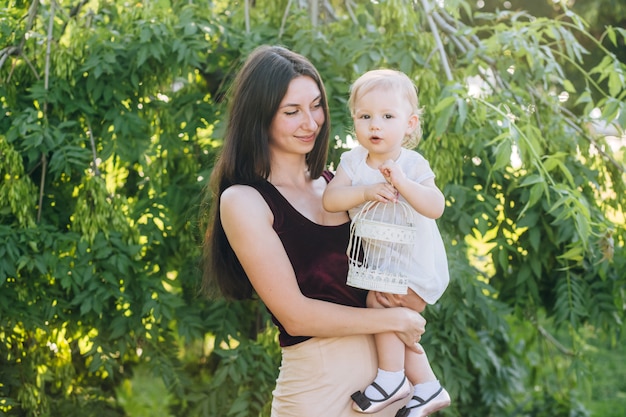 Mãe com um bebê nos braços em um dia ensolarado caminha pelo parque.