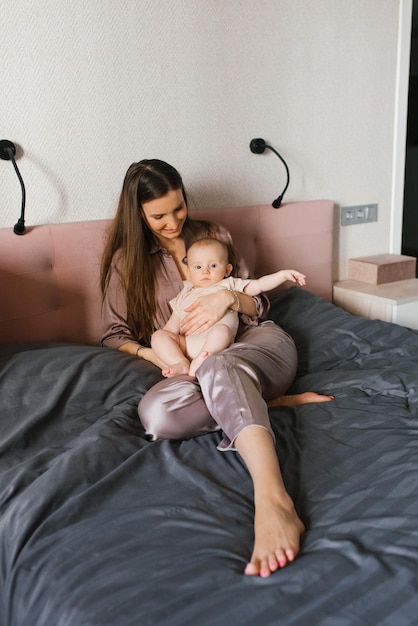 Mãe com um bebê nos braços senta-se no quarto na cama