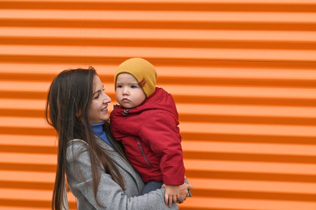 Mãe com um filho nos braços em roupas quentes em um fundo laranja