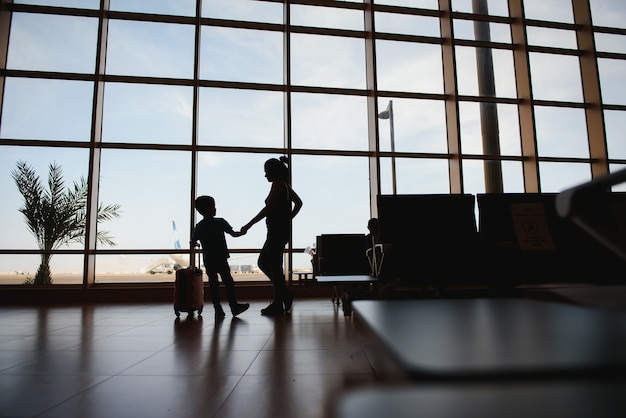 Mãe com um filho pequeno e uma mala no aeroporto.