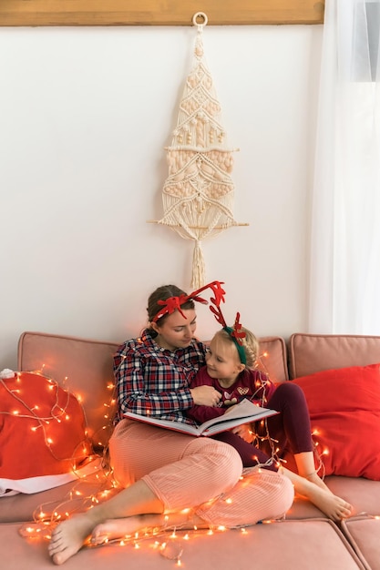 Mãe com uma filha de pijama e tiaras de natal com chifres de veado enquanto lia um livro mulher ...