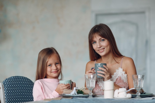 Mãe com uma filhinha sentar e tomar café da manhã à mesa na cozinha