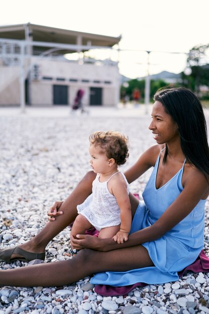 Mãe com uma garotinha sentada em uma praia de seixos