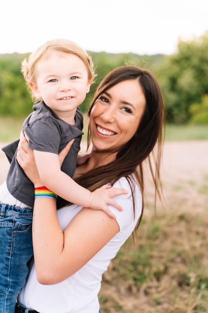 Mãe com uma pulseira lgbt segurando uma criança ao ar livre