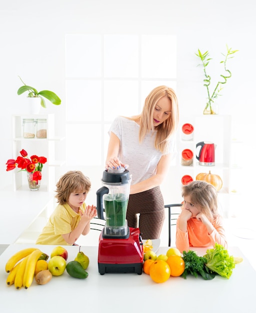 Mãe cozinha com filhos filha e filho na cozinha se divertem com smoothie verde Crianças se divertindo com alimentos vegetais na cozinha