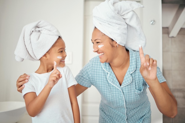 Mãe criança e cosméticos de creme de rosto para cuidados com a pele no banheiro em casa após a limpeza e higiene do chuveiro Mãe feliz sorria menina e bem-estar saudável com loção de beleza hidratante e massagem corporal