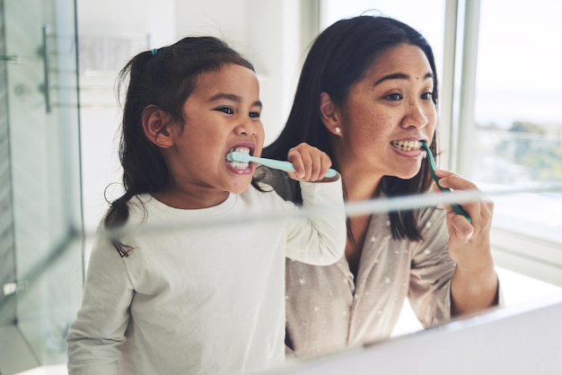 Mãe criança e escovar os dentes na rotina matinal de higiene de limpeza dentária ou cuidados de saúde juntos pelo espelho no banheiro Mãe feliz e boca de filha no clareamento dental cuidados orais ou gengivais em casa