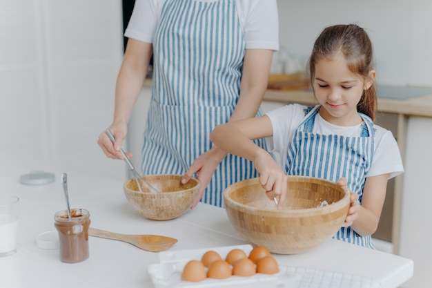 Mãe dá aula de culinária para criança pequena, fique ao lado do outro, misture o ingrediente em grandes tigelas de madeira