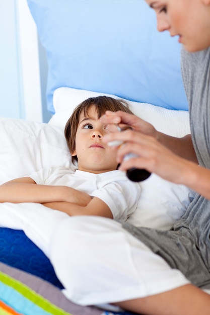 Mãe dando a seu filho deitado no xarope de cama