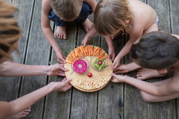 Mãe dando a seus filhos tábua de madeira com lanche vegetariano vegano