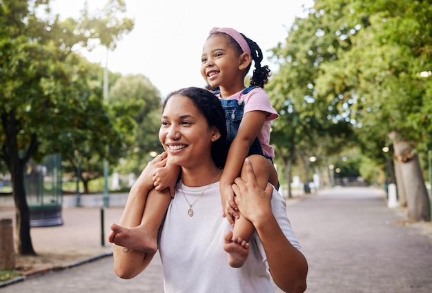 Mãe de costas com menina e no pescoço felicidade férias de verão e caminhada no parque para um fim de semana de união ou tempo de qualidade para se divertir Mamãe mamãe carrega uma criança do sexo feminino ou brincalhona sorri ou ama ao ar livre