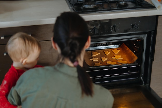 Foto mãe de família com bebê cozinhando pão de gengibre e colocando biscoitos no forno de natal caseiro