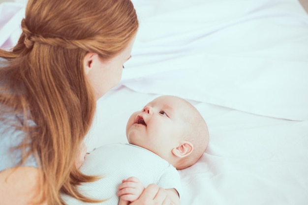 Mãe de família feliz brincando na cama com bebê recém-nascido