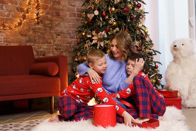 Mãe de família feliz com filhos na manhã de Natal de pijama perto de árvore de Natal com presentes caucasi ...